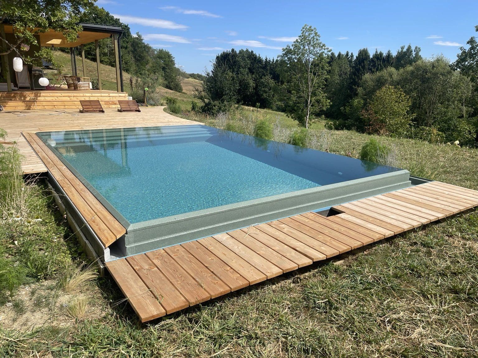 Massivpool mit Kaskadenrinne am Hang und freiem Blick in die Landschaft